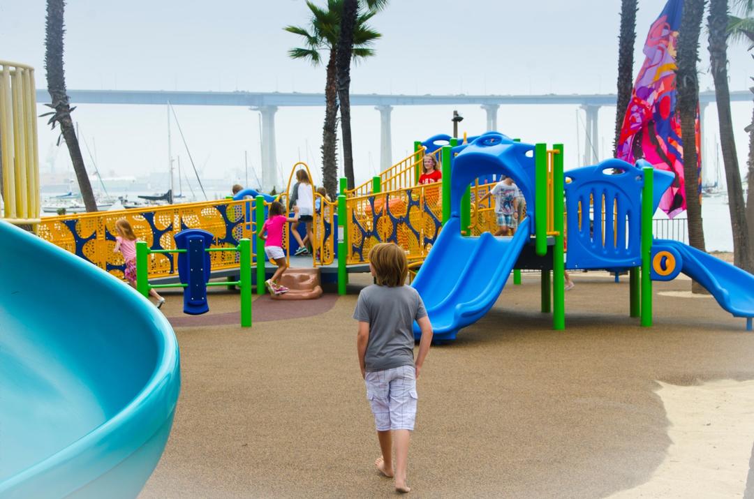 A boy child walks towards the colorful playground at Coronado Tidelands Park