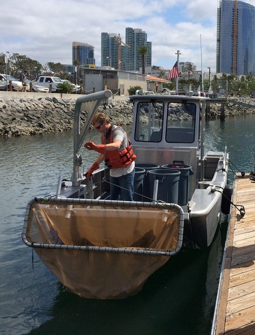 A worker lifts a net on a boat that is used to collect trash fromt he water.