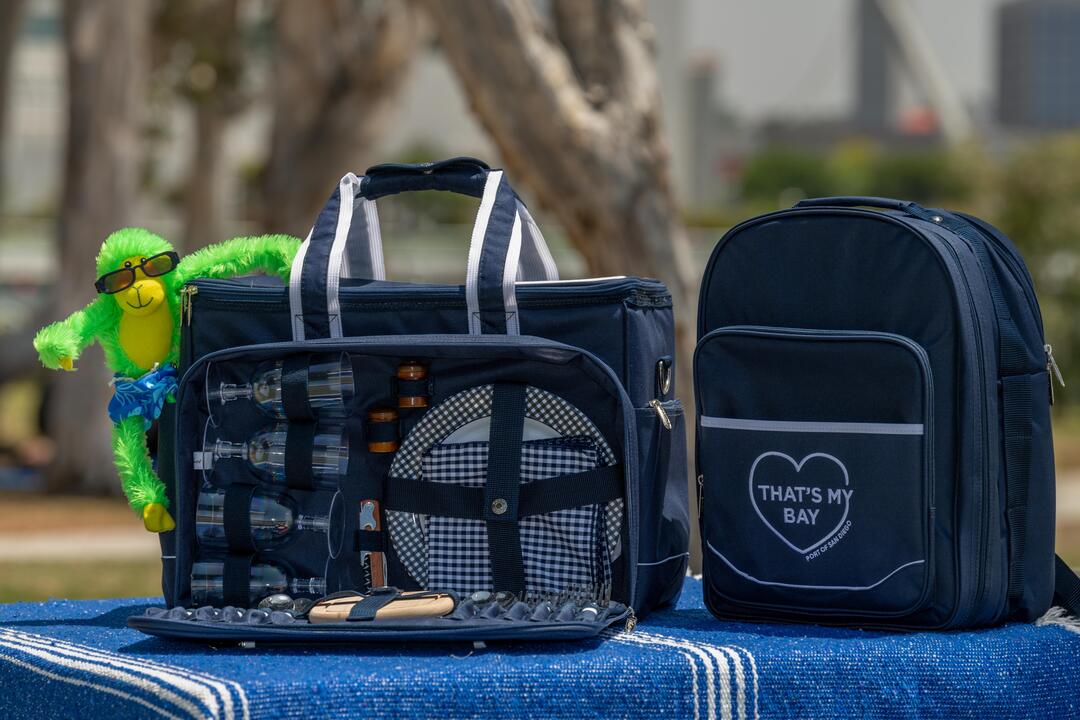 Two dark blue picnic totes, one is open and Hank, the green money, is hanging on!