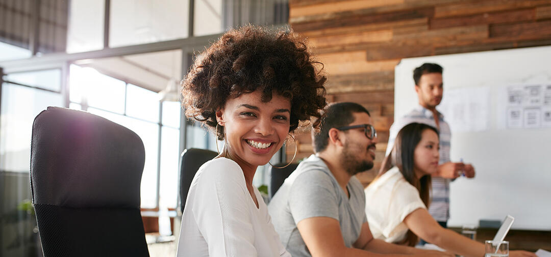 a Black woman smiles at the camera - colleagues in the background