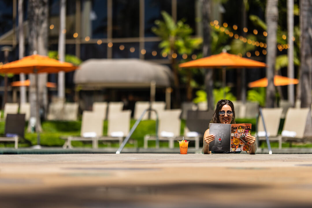 a woman is reading outside with orange umbrella in the background