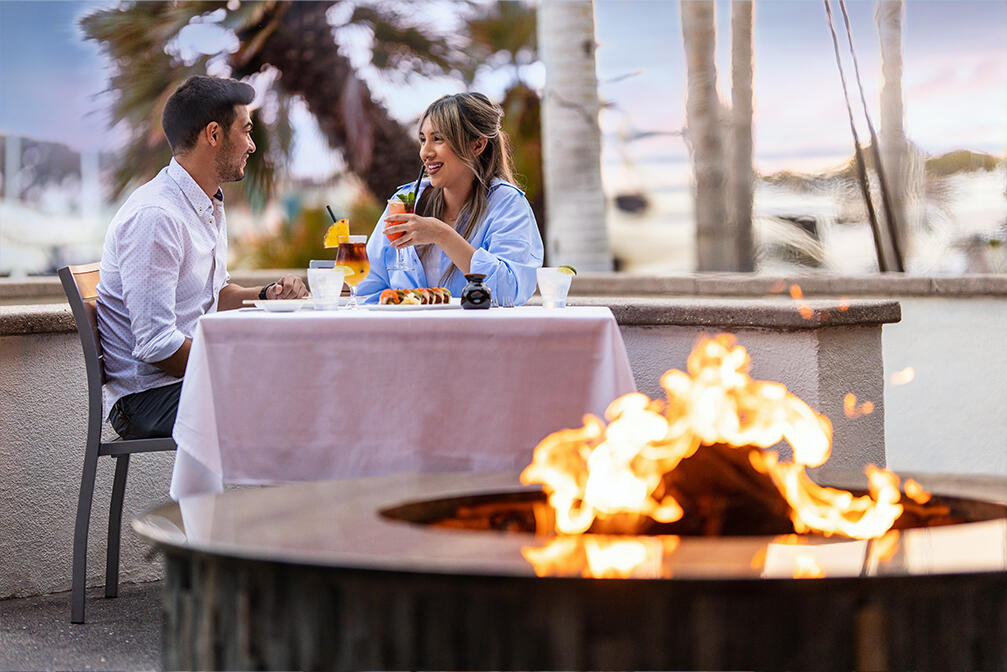 a couple sits in front of a fire at Roy's San Diego