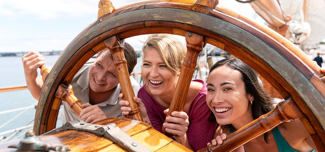 smiling people look through the spokes of a ship steering wheel