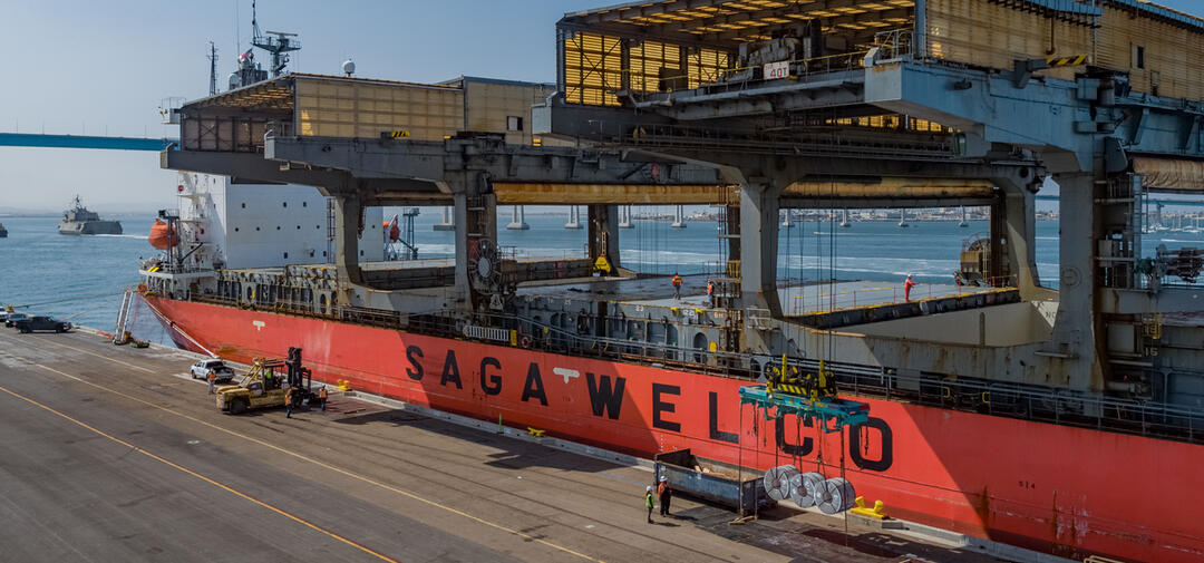 the huge, red & yellow, SAGA WELCO cargo ship is docked next to a large gray flat dock