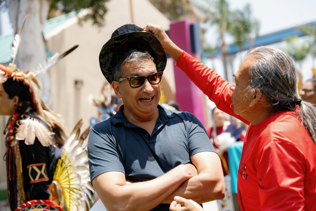 A man lifts a hat off of another's head