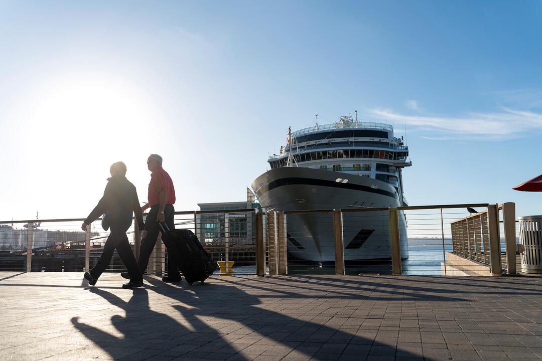 a couple with a suitcase walk in front a cruise ship along the Embarcadero