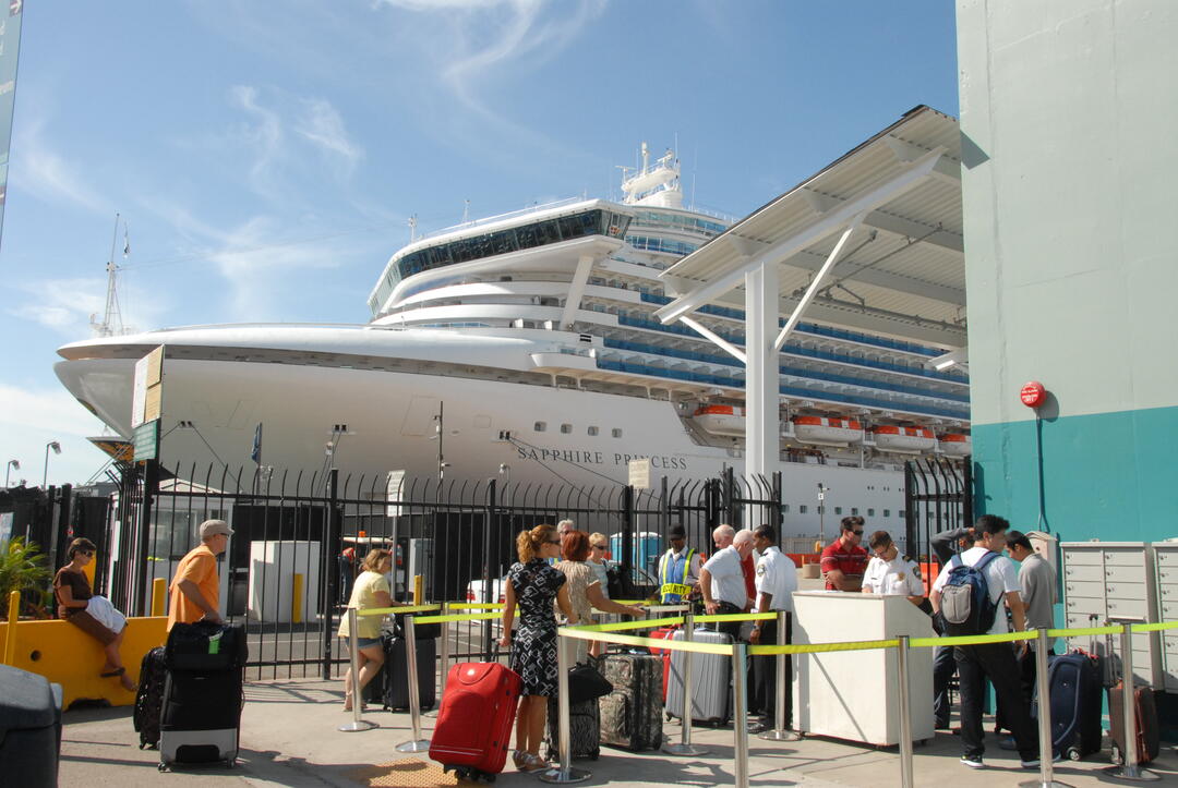 San Diego Bay visitors with luggage waiting in line to enter the Port of San Diego cruise terminal with a cruise ship in the background.