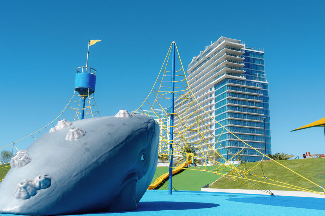 Image of grey Humpback whale climbing structure and other yellow and blue playground. equipment with Gaylord Hotel in the background