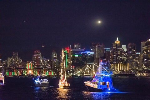 Boats with colorful lights on the water with the skyline in the background.