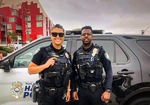 A female and male police officer from Port of San Diego Harbor Police standing in front of a patrol vehicle.