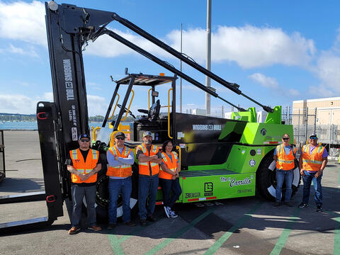 people in orange safety vest stand around a new electric forklift