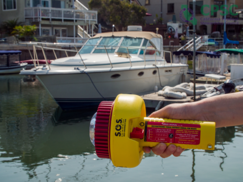 Marine flare in someone's hand with water and a boat in the background.
