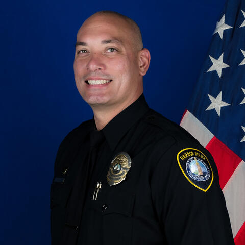 Headshot of Officer Collier with the Port of San Diego Harbor Police Department has a blue background with a flag of the USA on the right.