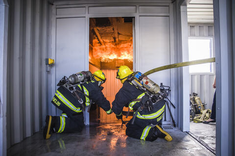 Two Harbor Police Officer in firefighting gear training to fight fires on the fire simulator barge with flames inside the barge.