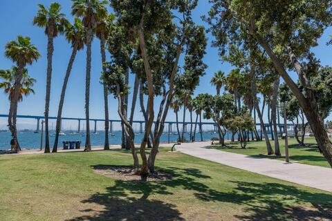Image of trees, grass and a pedestrian walkway looking toward the blue Coronado Bridge in Tidelands Park in Coronado along San Diego Bay.
