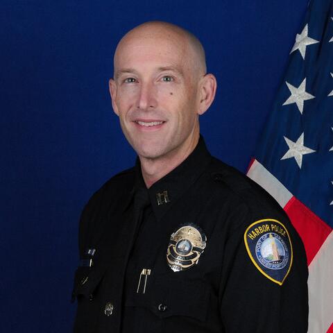 Photo of Harbor Police Captain Jonathan George against a blue backdrop with an American flag.