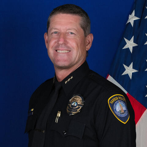 Photo of Harbor Police Assistant Chief Jeff Geary against a blue backdrop with an American flag.
