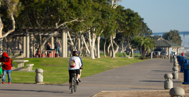 person on bike riding away from viewer on a path next to San Diego bay