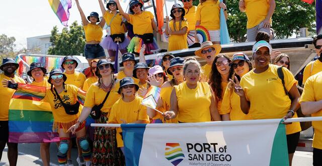 Port employees in yellow shirts and colorful accessories pose behind a Pride Parade banner.