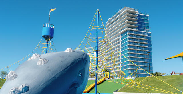 Image of grey Humpback whale climbing structure and other yellow and blue playground. equipment with Gaylord Hotel in the background