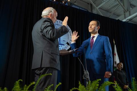 Commissioner Emeritus Garry Bonelli stands with his right hand up in front of Chairman Rafael Castellanos who also has his right hand raised. Bonelli is swearing Castellanos in as the 2023 Chairman of the Board of Port Commissioners.