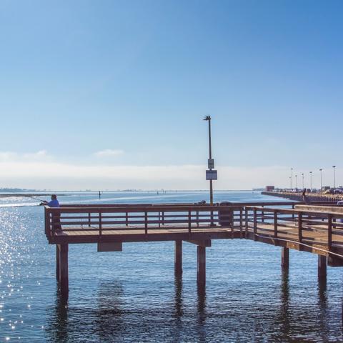 Man fishing off the fishing pier on a sunny day with blue skies and glistening water at Pepper Park at the Port of San Diego