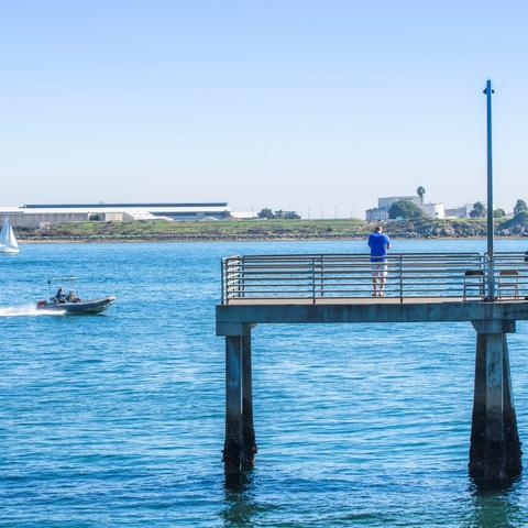 Man taking a photo from the pier of the speedboat on the bright blue water under light blue skies