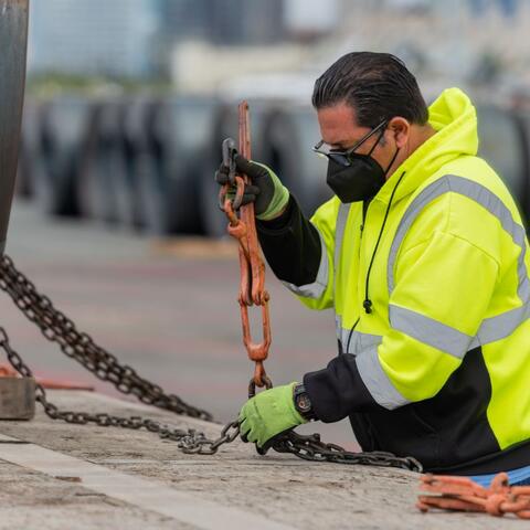 A man in a bright yellow jacket works with a chain