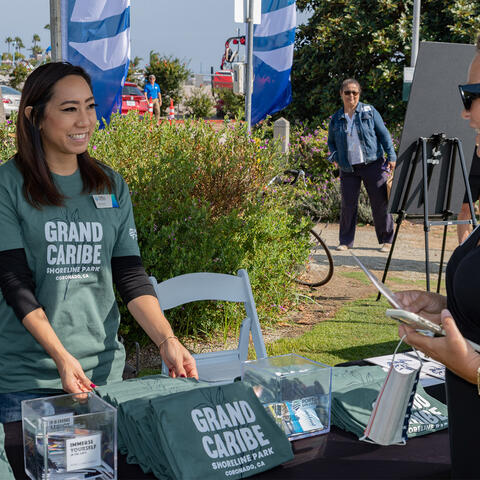 Port staff smiles & offers a t-shirt to a community member standing in front of a booth 