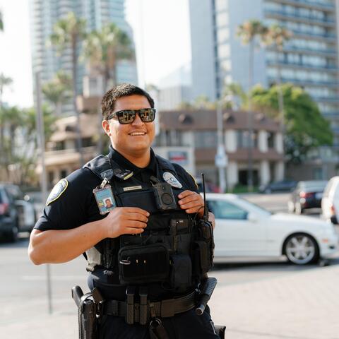 A uniformed San Diego Harbor Police Officer smiles. The city and traffic are in the background.