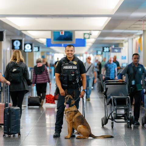 A Harbor Police K9 Officer stands with his dog in a busy airport hall